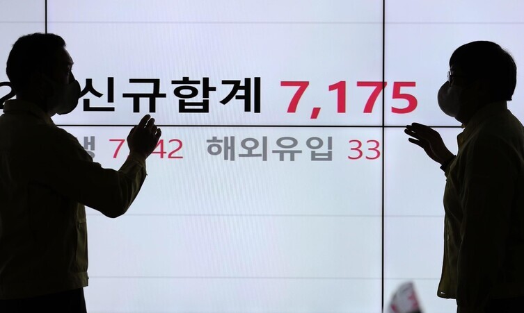 Silhouettes of two people can be seen in front of a screen at the Songpa District Office in Seoul showing the number of COVID-19 cases confirmed by the end of Tuesday, when Korea first recorded a daily caseload in the 7,000s, on Wednesday. (Kang Chang-kwang/The Hankyoreh)