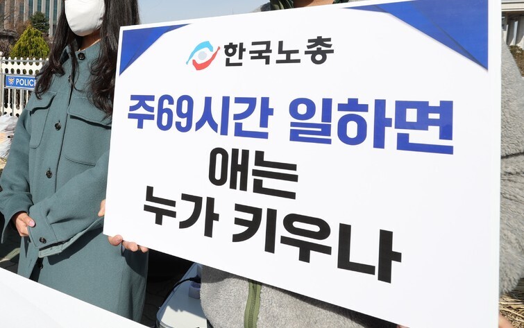 A participant in a press conference held jointly by the KCTU, the Democratic Party, and the Justice Party outside the National Assembly on March 16 holds a sign reading, “Who’ll raise the kids if we’re working 69 hours per week?” (Kim Jung-hyo/The Hankyoreh)