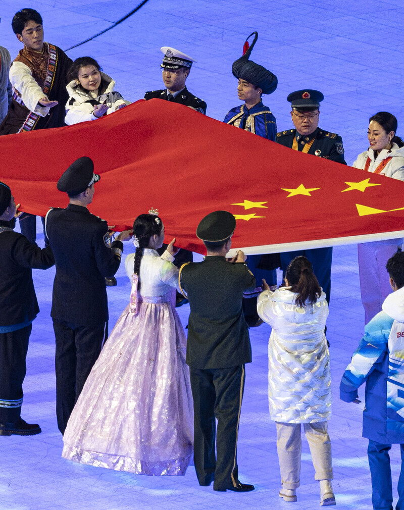 During Friday’s opening ceremony for the 2022 Beijing Winter Olympics, a woman dressed in a hanbok with a daenggi ribbon in her hair helps convey the Chinese flag to the flagpole. (Yonhap News)