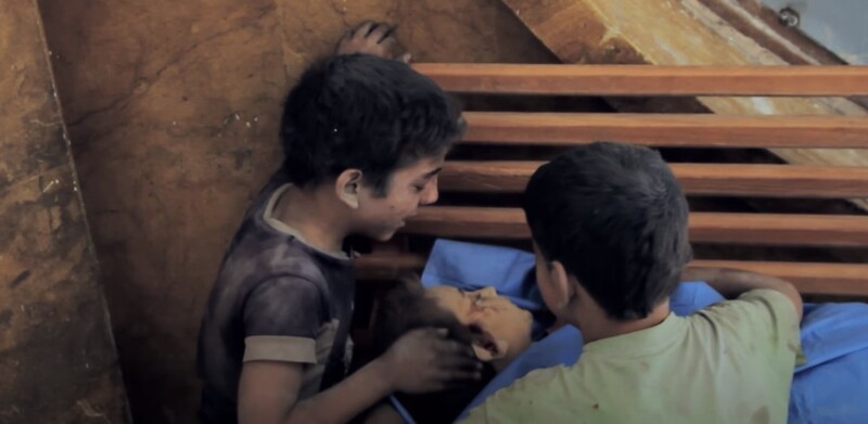 시리아의 두 아이가 폭격으로 목숨을 잃은 동생의 얼굴을 어루만지고 있다. 다큐멘터리 <사마에게> 갈무리