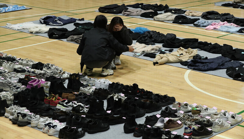 Two people crouch and cry on the floor of a gymnasium in Seoul where items found in the aftermath of the Itaewon disaster were laid out on Nov. 1, 2022. (Kim Jung-hyo/The Hankyoreh)