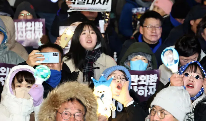 Participants in a rally outside the front gates of the National Assembly in Seoul’s Yeouido on Dec. 3, 2025, wave light sticks and chant slogans as they mark the one-year anniversary of the attempted self-coup by Yoon Suk-yeol, who was later impeached and deposed. (Yoon Woon-sik/Hankyoreh)