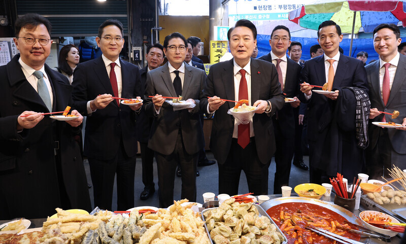 President Yoon Suk-yeol of South Korea (fourth from left) eats tteokbokki with business bigwigs at a market in Busan on Dec. 6. From left to right: SK Group Executive Vice Chairperson Chey Jae-won, Samsung Electronics Executive Chairperson Lee Jae-yong, Hyosung Group Chairperson Cho Hyun-joon, Yoon, LG Group Chairperson Koo Kwang-mo, Hanwha Group Vice Chairperson Kim Dong-kwan and HD Hyundai Group Vice Chairperson Chung Ki-sun. (Yonhap)
