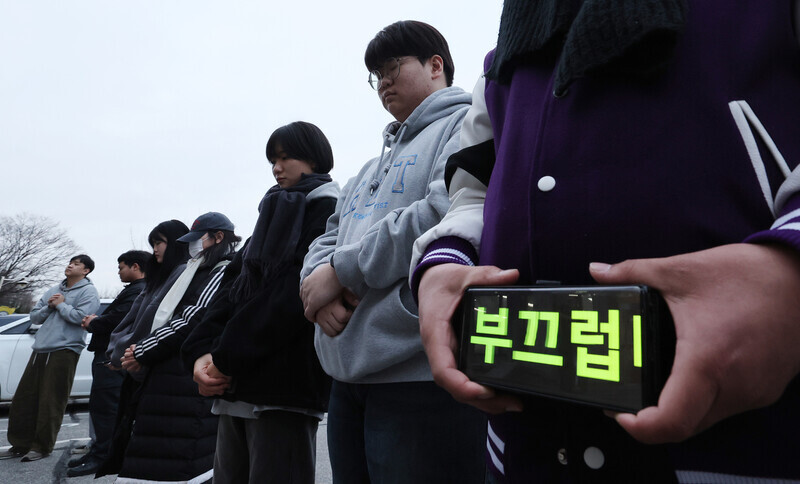 “Shameful” reads a message on a phone held by a Hanshin University student participating in a prayer gathering at the school’s Gyeonggi campus in Osan on Dec. 13 to denounce the forced expulsion of international students from the country. (Shin So-young/The Hankyoreh)