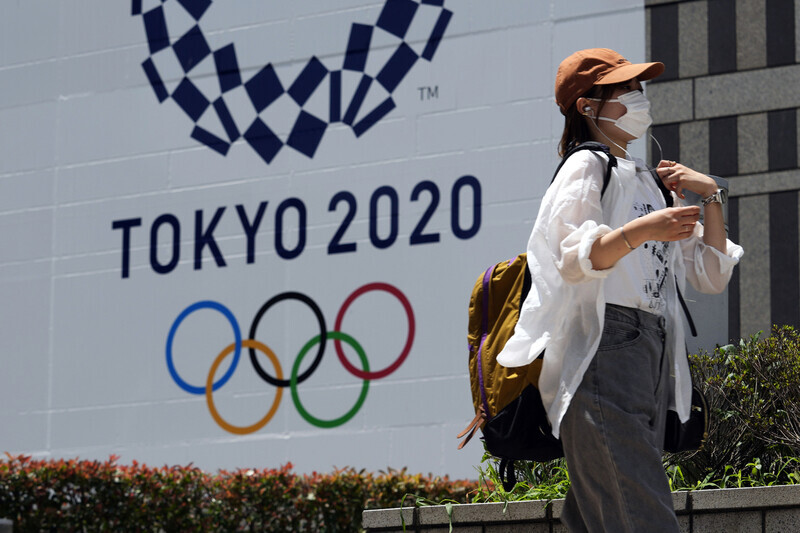 A person wearing a protective mask walks past an Olympics banner hung up outside the Tokyo Metropolitan Government building in Tokyo on Tuesday. (AP/Yonhap News)