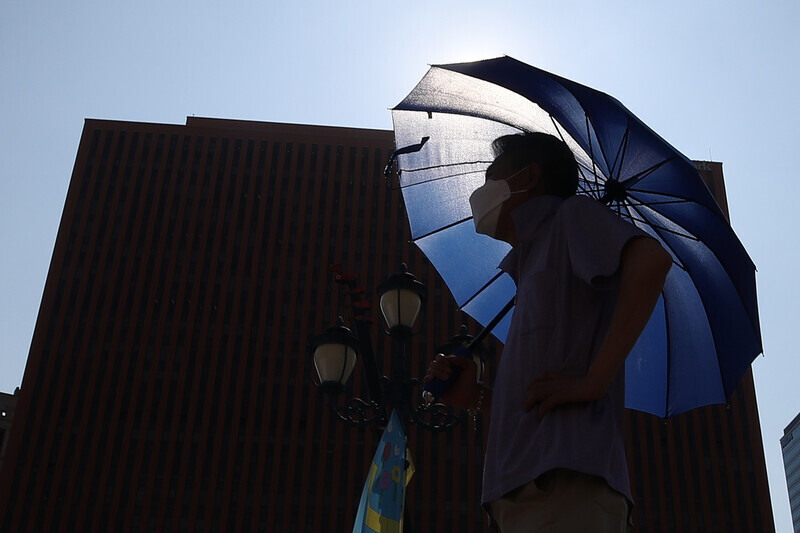 A person waits in line to get tested for COVID-19 at a temporary screening station in Seoul with a parasol in their hand on Tuesday. (Yonhap News)