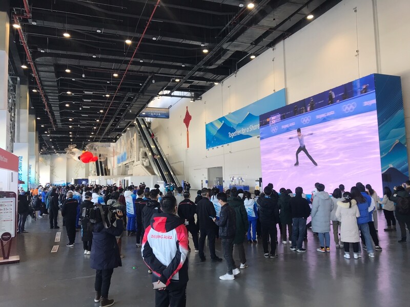 世界中のジャーナリストとボランティアが、中国の北京にあるメインメディアセンターの1階に設置された大画面で、男子フィギュアスケートのショートプログラムで羽生のパフォーマンスを見る。8。北京/レポーターJunhee Lee
