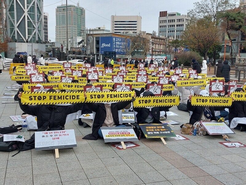 Participants in Haeil’s rally calling for stronger punishment of violent crimes against women hold up signs reading “Stop femicide” in English and funeral signs suggesting “they died because they were women” as they sit near the Bosingak belfry on Dec. 4. (Oh Se-jin/The Hankyoreh)
