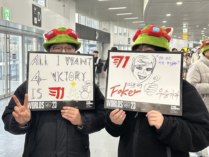 Kang Min-hyeok (left) and Jeong Gyeong-tae (right) hold up signs cheering on T1 in the LoL World Championship finals held at Gocheok Sky Dome on Nov. 19. (Chung In-seon/The Hankyoreh)