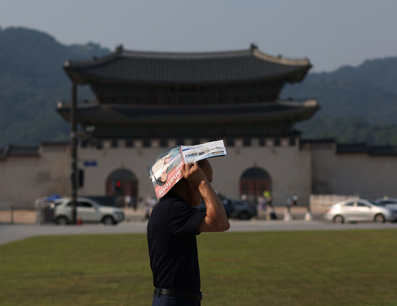 A pedestrian shields himself from the sun with a brochure as he walks through the streets of Seoul's Gwanghwamun on June 19, 2024, during a heat advisory. (Yonhap)