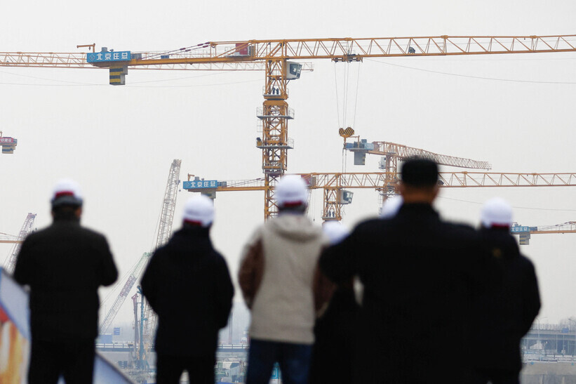 Workers watch cranes in action at a construction site in Beijing, China, on Jan. 12. (Reuters/Yonhap)