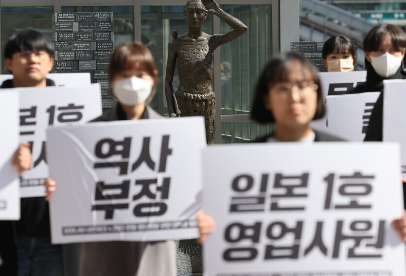 Members of the Peace Nabi Network, a network of university students seeking a resolution to the Japanese military’s system of sexual slavery, hold up signs condemning the Korea-Japan summit and rejecting the Yoon administration’s “degrading” solution to the issue of compensation for forced laborers in front of a monument to forced laborers in the plaza outside Yongsan Station in Seoul on March 16. Visible signs read “Japan’s No. 1 salesman” and “Denial of history.” (Yonhap)