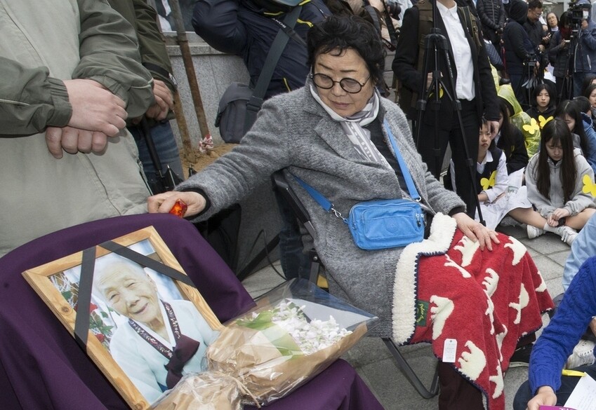 Former comfort woman Lee Yong-su strokes a chair with a portrait of former comfort woman Lee Soon-deok