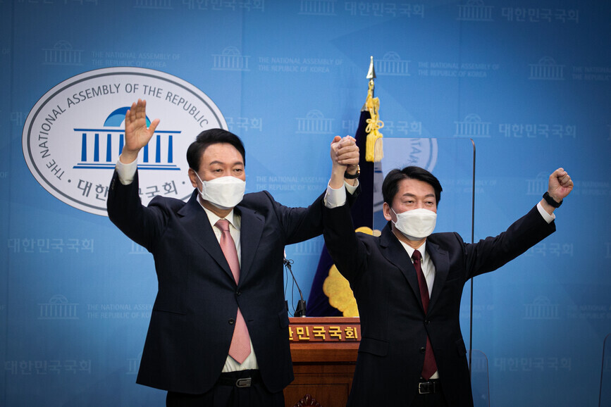 Ahn Cheol-soo and Yoon Suk-yeol raise their hands together at a press briefing on March 3 at the National Assembly building in Seoul’s Yeouido neighborhood announcing that Ahn has dropped out to endorse Yoon’s bid for president. (Yonhap News)