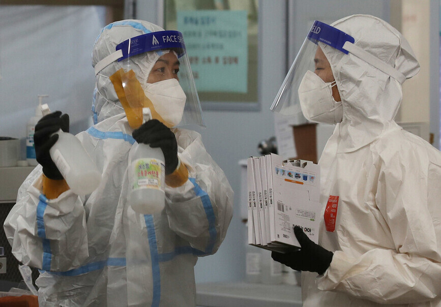 Two workers at the Songpa Health Center in Seoul converse on Nov. 28, one having sealed their protective attire with tape. (Baek So-ah/The Hankyoreh)