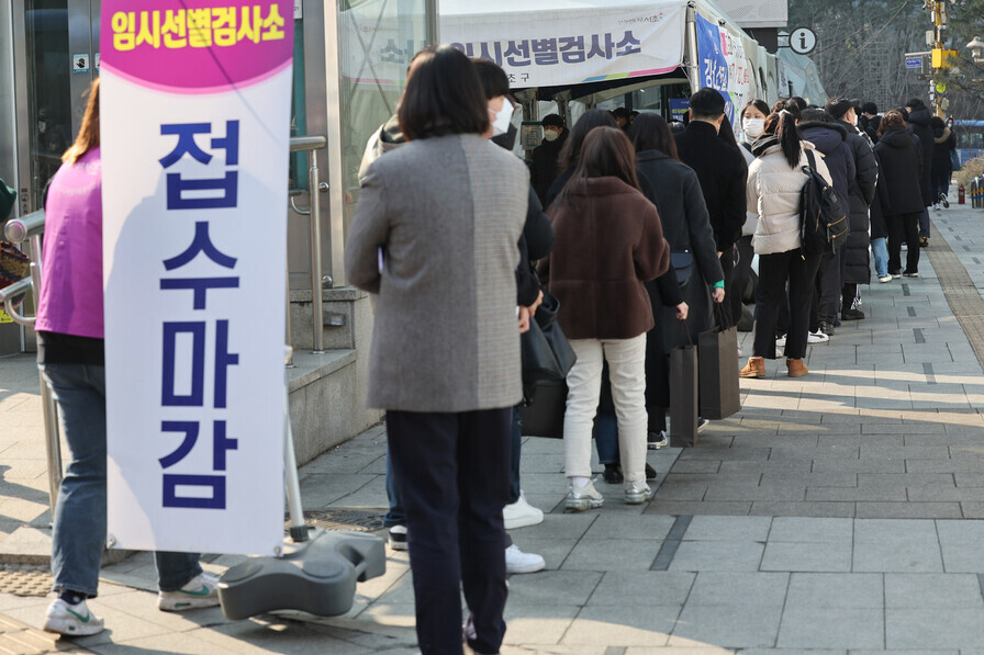 As people wait to be tested for COVID-19 at a temporary screening station near Gangnam Station in Seoul on Wednesday, a worker carries out a sign saying that they’re stopping testing for the day. (Yonhap News)