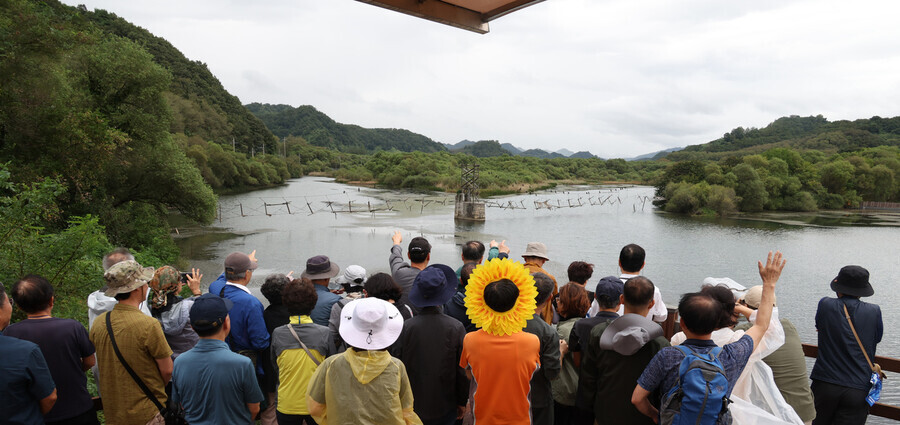 Participants in the Hankyoreh’s “DMZ ecology and peace tour” on Sept. 15 peer at the Yongyang Reservoir at the DMZ ecological peace park in Cheorwon County on Sept. 15. Over the reservoir, the dilapidated remains of a suspension bridge used by border guards after the war can be seen. (Kang Chang-kwang/The Hankyoreh)