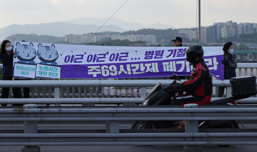 Members of the Korean Confederation of Trade Unions hold a banner calling on the Yoon Suk-yeol administration to scrap its plans for a 62-hour workweek on Wonhyo Bridge in Seoul on April 26. (Yonhap)