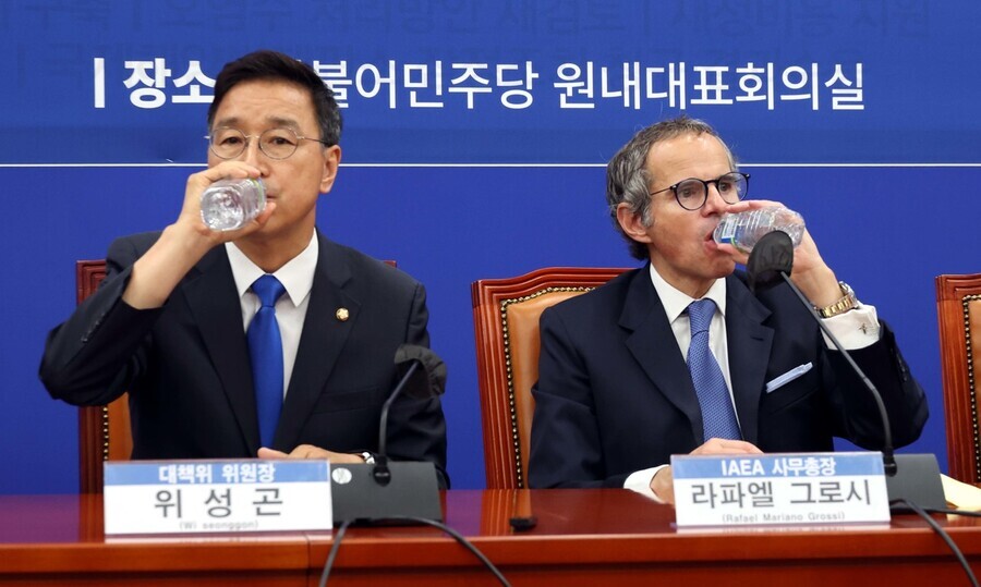 Wi Seong-gon, who chairs the Democratic Party’s task force on the discharge of contaminated water from the Fukushima nuclear plant, and IAEA Director General Rafael Grossi each take a sip of bottled water during a meeting with Democratic lawmakers on the task force at the National Assembly in Seoul on July 9. (pool photo)