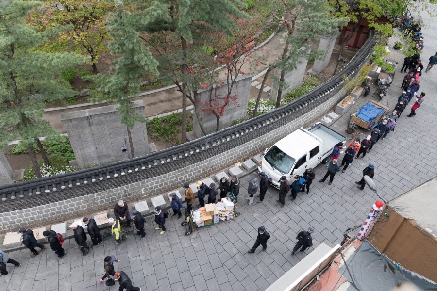 서울 종로 원각사 무료급식소를 찾은 어르신들이 4월20일 탑골공원 담장을 따라 길게 늘어서 있다. 반드시 마스크를 써야 하고 체온 측정과 소독을 거친 뒤 음식을 받을 수 있다.