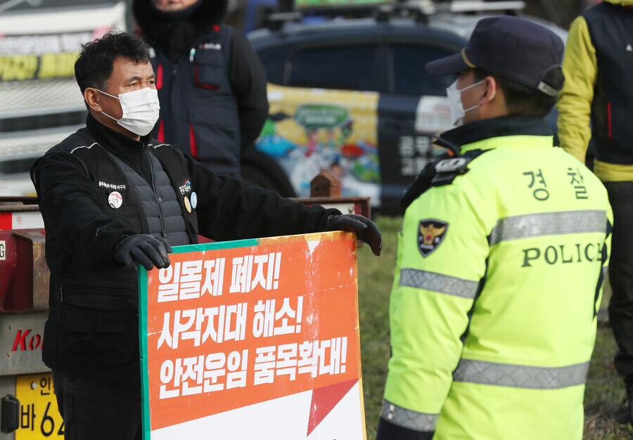 A member of the Cargo Trucker Solidarity Division holds a sign with three of the union’s demands — abolition of the sunset clause of a minimum pay system, reduction of blind spots, expansion of minimum pay system to other cargo types — while a police officer confronts him. (Yonhap)