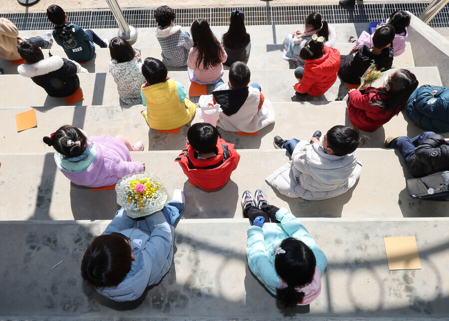 Students from Taerang Elementary School in Seoul sit on their school’s steps during their commencement ceremony on March 2. (Yonhap)