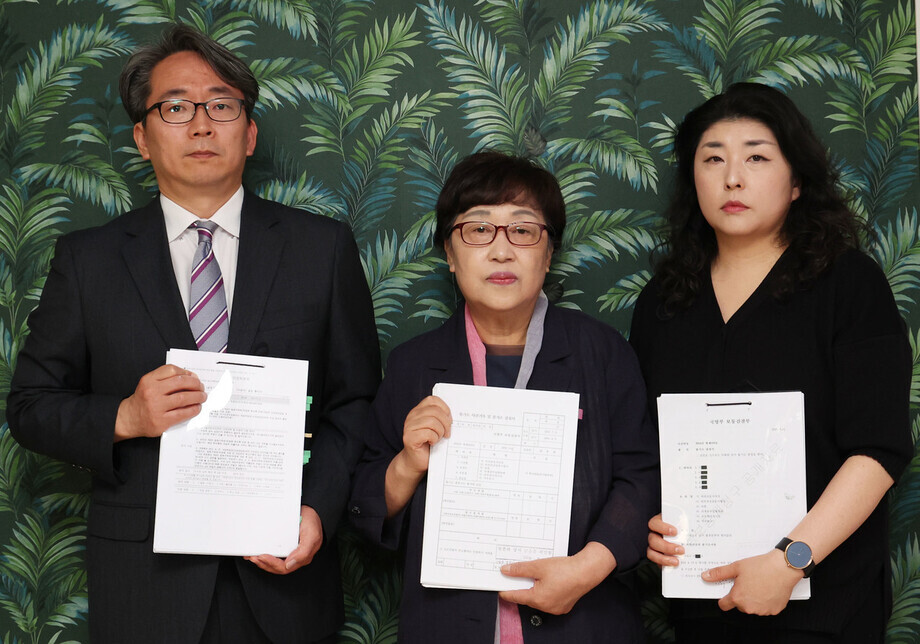 Family of the late soldier Yoon Seung-ju hold up court records and related documents acquired through an information disclosure request ahead of speaking to the Hankyoreh at its offices in Seoul on May 1, 2024. From left to right are Yoon’s elder brother-in-law Kim Jin-mo, Yoon’s mother Ahn Mi-ja, and Yoon’s older sister Yun Seon-yeong. (Baek So-ah/The Hankyoreh)