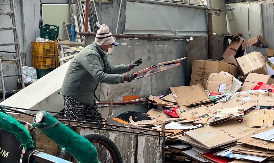 An older Korean takes cardboard boxes out of his card at a junkyard in Seoul’s Yeongdeungpo neighborhood on Dec. 12. (Lee Woo-yun/The Hankyoreh)