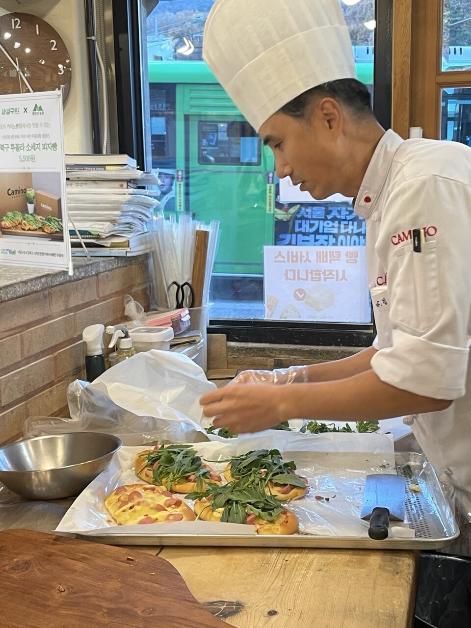 까미노빵집 김영국(51) 사장이 ‘루꼴라 소시지 야채피자빵’(5500원)을 만들고 있다. 강북 스마트팜에서 저렴하게 납품받은 덕에 루꼴라를 푸짐하게 올리고 있다.