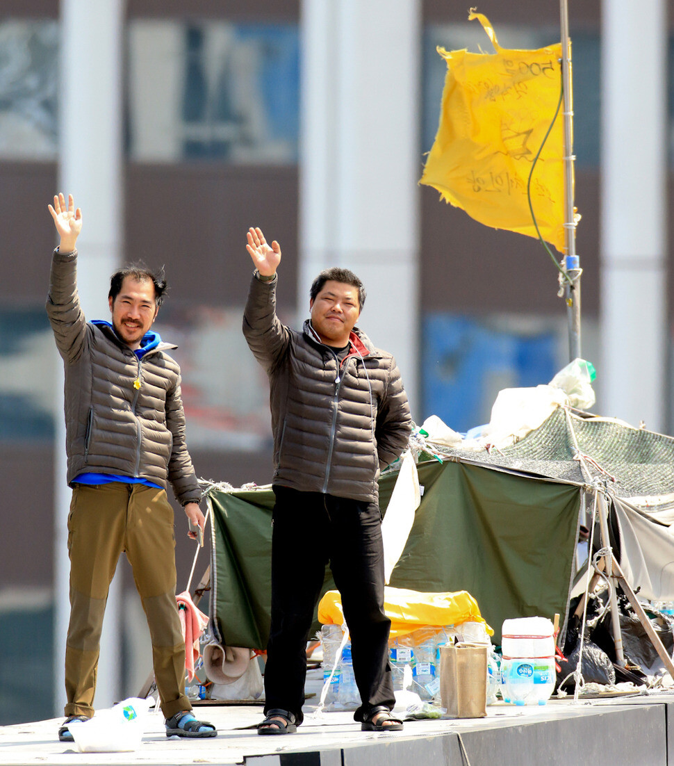 Irregular Kia Motors workers Choi Jeong-myeong (left) and Han Gyu-hyeop wave from an advertising space atop the National Human Rights Commission building in central Seoul
