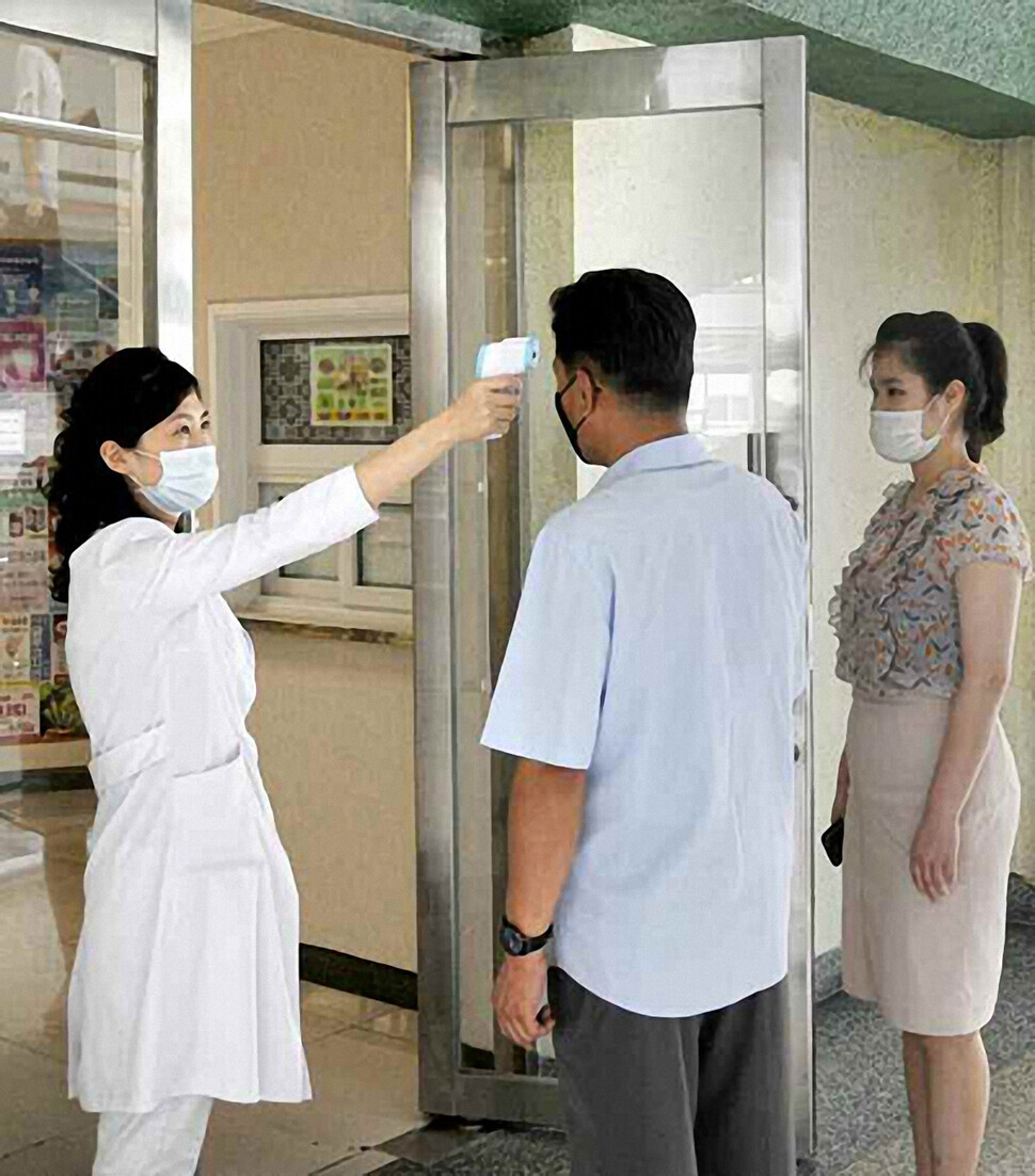 This photo, published in the North's state-run Rodong Sinmun newspaper in August 2020, shows a health worker administering a temperature check on a man in Pyongyang. (Yonhap News)