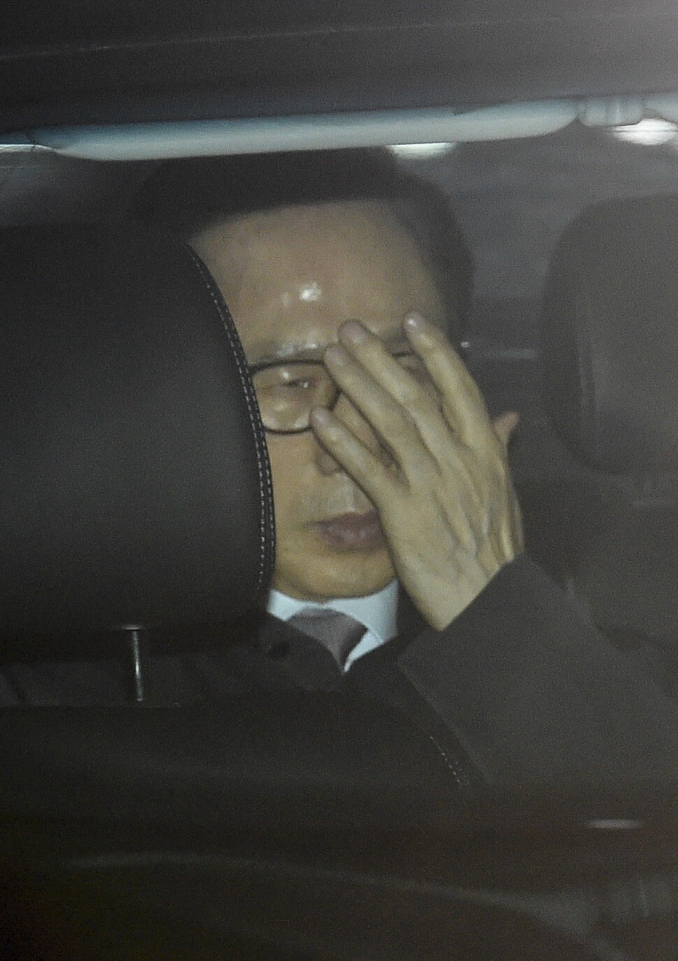 Former president Lee Myung-bak covers his face as he is taken to the Seoul Eastern Detention Center from his home in the Nonhyeon neighborhood in Seoul on the morning of Mar. 22. (Photo Pool)