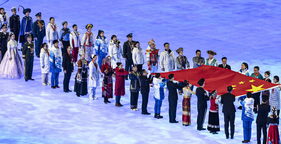 Members of China’s various ethnic groups dressed in their respective heritage attire help convey the Chinese flag during the opening ceremony of the Beijing Winter Olympics on Friday. The second person from the left in the closer row is a Korean Chinese woman. (Yonhap News)