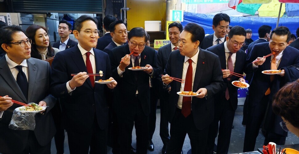 President Yoon Suk-yeol of South Korea (fourth from left) eats tteokbokki with business bigwigs at a market in Busan on Dec. 6. From left to right: SK Group Executive Vice Chairperson Chey Jae-won, Samsung Electronics Executive Chairperson Lee Jae-yong, Hyosung Group Chairperson Cho Hyun-joon, Yoon, LG Group Chairperson Koo Kwang-mo, Hanwha Group Vice Chairperson Kim Dong-kwan and HD Hyundai Group Vice Chairperson Chung Ki-sun. (Yonhap)