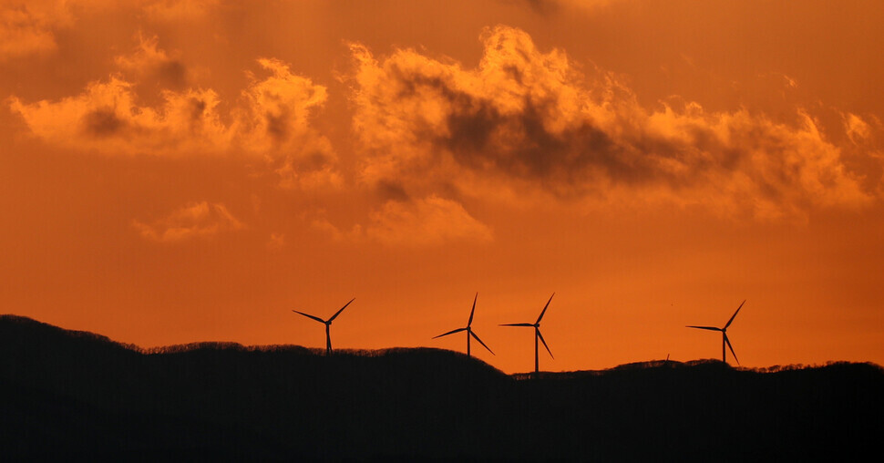Silhouettes of wind turbines stand in the foreground of glowing orange sunset over the Baekdu-Daegan mountain system on Feb. 19. (Yonhap News)