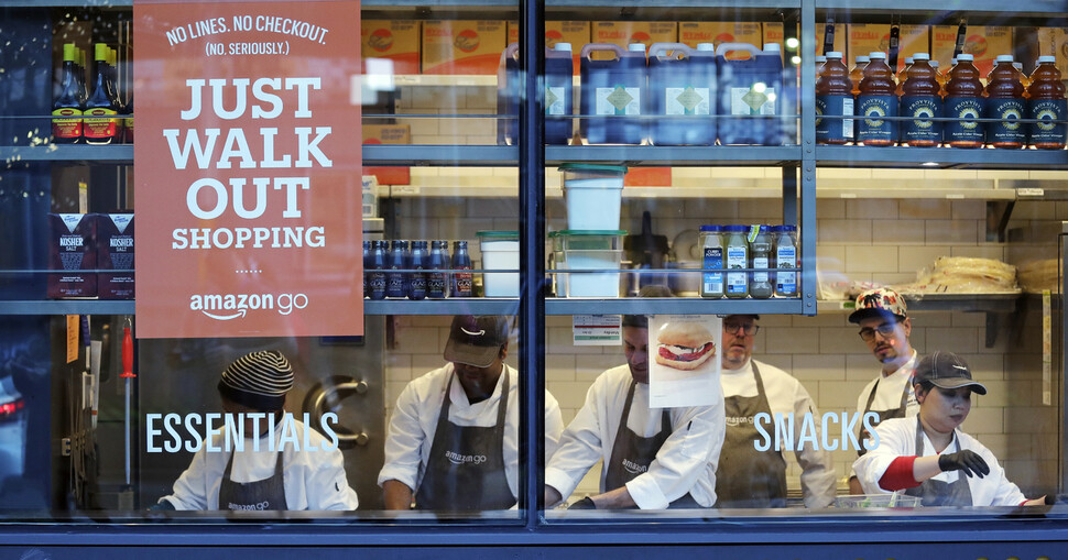 미국 시애틀의 한 아마존 고 매장에서 노동자들이 샌드위치를 만들고 있다. 매장 창문에 ‘저스트 워크 아웃 쇼핑’이라는 공지가 붙어 있다. AP 연합뉴스