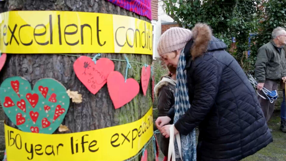 다큐멘터리영화 ‘더 펠링’(The Felling·베어짐)의 한 장면. 한 주민이 ‘엄청 건강한 상태’ ‘기대수명 150년’이라고 쓰인 펼침막을 나무에 두르고 있다.