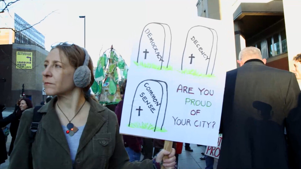 다큐멘터리영화 ‘더 펠링’(The Felling·베어짐)의 한 장면. 한 주민이 ‘당신의 도시가 자랑스럽나요?’라고 적힌 손팻말을 들고 있다. 민주주의와 존중, 상식이 죽었다는 내용의 삽화도 그려져 있다.