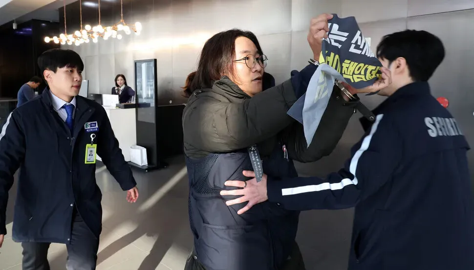 A unionist in handcuffs holds up a banner calling for corporate accountability for deaths at Coupang distribution centers during a surprise demonstration at the e-commerce giant’s headquarters in Seoul’s Songpa District on Dec. 10, 2025. (Kim Young-won/Hankyoreh)