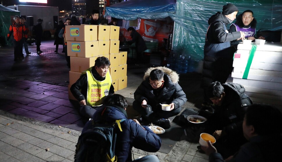 서울 광화문에서 농성 중인 노동자들이 식사하는 동안 뒤편에 ‘꿀잠’이 보낸 김장이 쌓이고 있다.