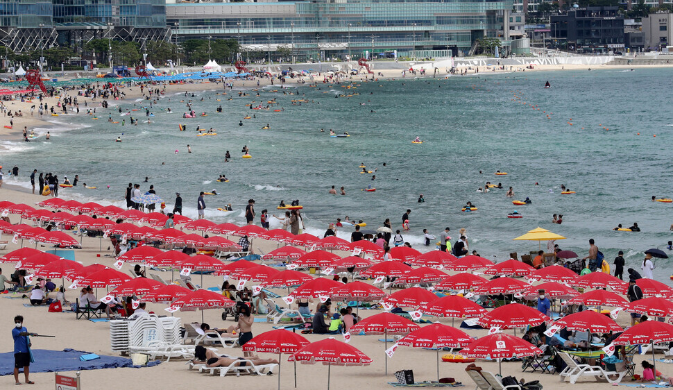 People avoid the heat under parasols on Haeundae Beach in Busan on Sunday. (Yonhap News)