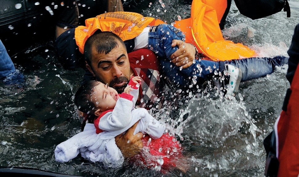 한 시리아 난민이 2015년 9월24일 터키에서 에게해를 건너 그리스 레스보스섬에 도착해, 배에서 내리다 넘어져 아이가 물에 빠지자 놀라 붙잡고 있다.