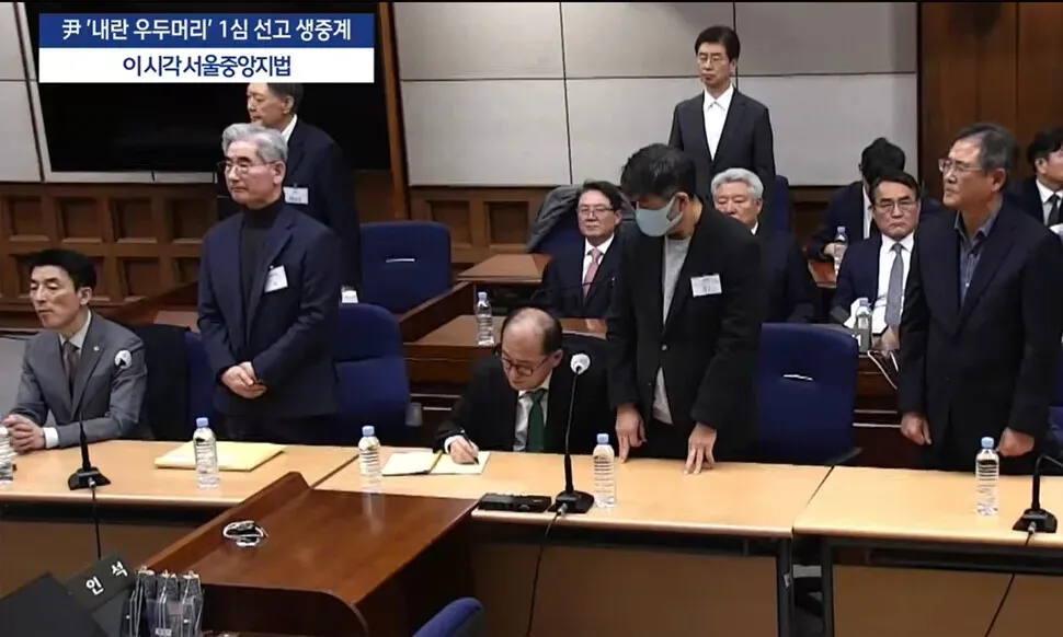 Former President Yoon Suk-yeol (second from left, back) and former Defense Minister Kim Yong-hyun (second from left, front) stand as the Seoul Central District Court reads its verdict in their insurrection trials on Feb. 19, 2026. (still from courtroom live stream)