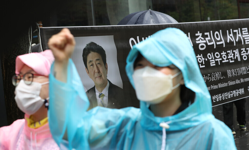A participant in the Wednesday Demonstration on July 13 in downtown Seoul holds up their hand in the foreground as a memorial banner for Shinzo Abe hangs in the background. (Kang Chang-kwang/The Hankyoreh)