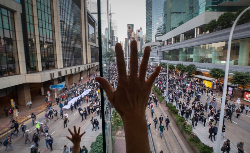 시민들이 행진하는 도로를 가로지른 쇼핑몰 연결통로에서 아이와 함께 쇼핑을 나온 한 시민이 시위대를 향해 다섯 손가락을 펼쳐 보이며 연대와 지지 의사를 밝히고 있다.