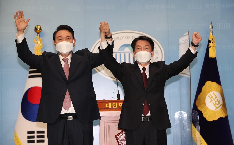 People Power Party presidential nominee Yoon Suk-yeol clasps hands with People’s Party presidential candidate Ahn Cheol-soo after a press conference at the National Assembly building in Seoul announcing they had merged their campaigns on March 3. (Kim Bong-gyu/The Hankyoreh)