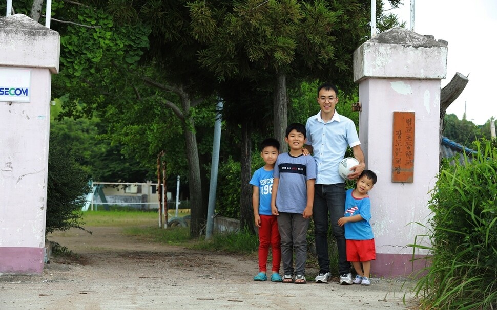 벌교초등학교 장도분교장의 유일한 학생 6학년 김이건(왼쪽 둘째)이 김성현 교사와 교문 앞에 섰다. 맨 왼쪽은 김 교사의 큰아들 강유, 맨 오른쪽은 둘째 신유.