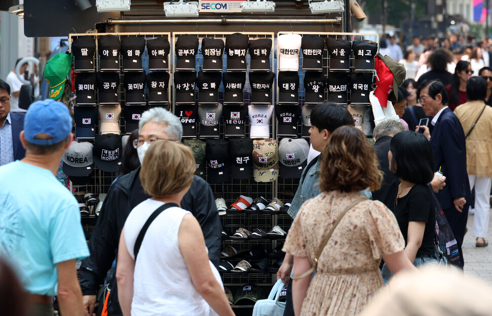 ‘곧부자’ ‘회장님’ 등 사회적 역할부터 ‘엄마' ‘아빠’ ‘귀한자식’ 등 가정의 역할까지 새겨진 모자를 팔고 있는 서울 중구 명동 거리의 한 노점 주변에서 2025년 5월27일 외국인 관광객과 시민들이 이를 살펴보고 있다.