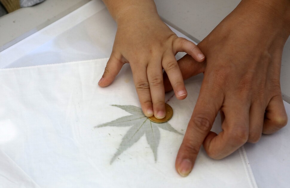 행사에 참가한 어머니와 아이가 손수건을 만드는 모습. 흰색 면수건에 나뭇잎을 놓고 동전으로 비벼 물들였다.