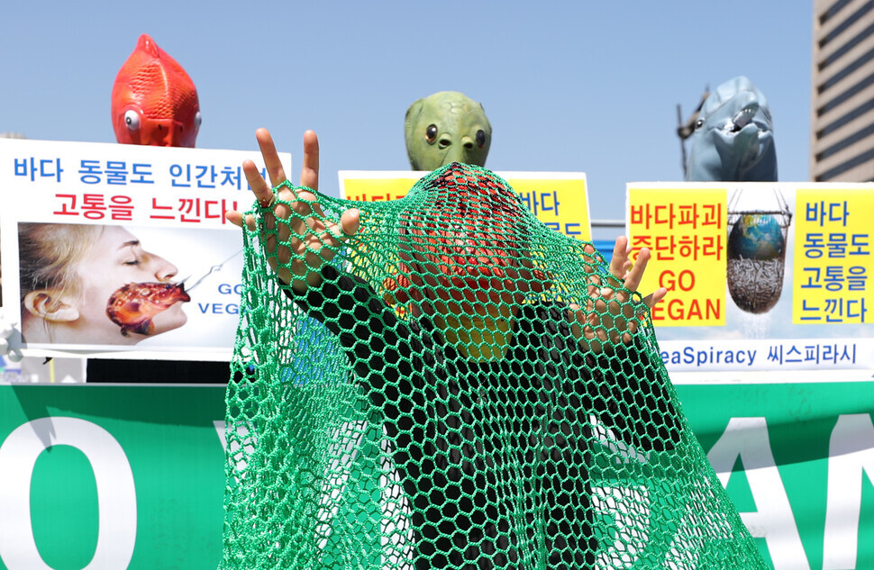 One of the protesters wearing a fish mask pretends to be a fish in a fishing net in a street performance staged after the press conference. (Lee Jong-keun/The Hankyoreh)